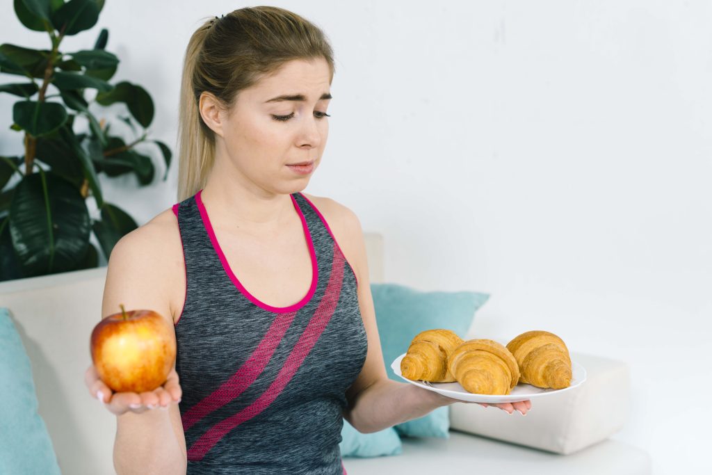 Woman deciding between healthy fruit and unhealthy pastries while making a balanced nutrition choice.