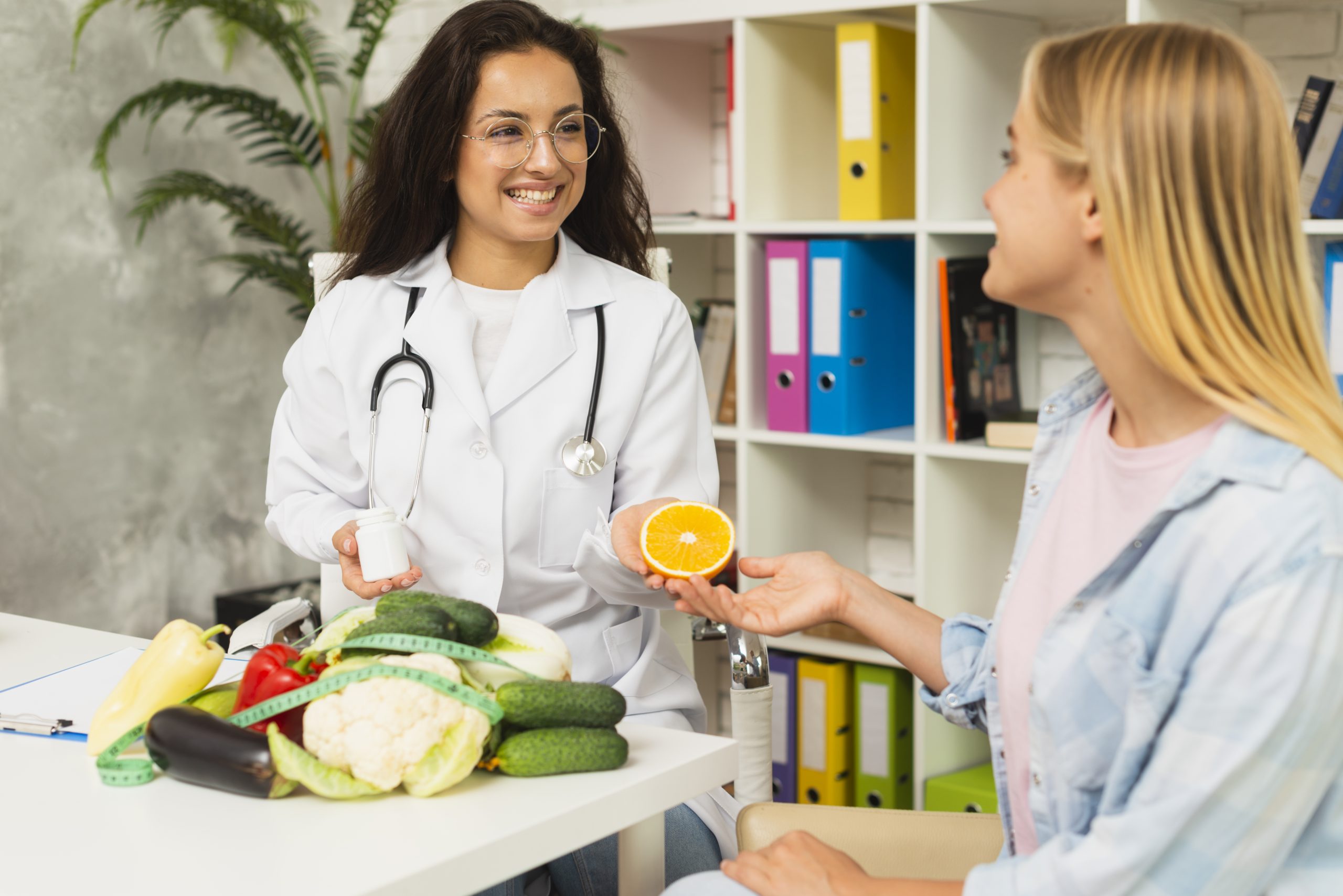 Doctor discussing healthy eating with a woman, showing fresh vegetables and a sliced orange.